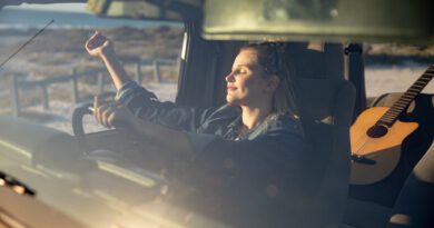 Vorderansicht einer kaukasischen Frau in einem offenen Top-Auto, hält ein Lenkrad, hob ihre Hände und entspannt in der Sonne mit geschlossenen Augen