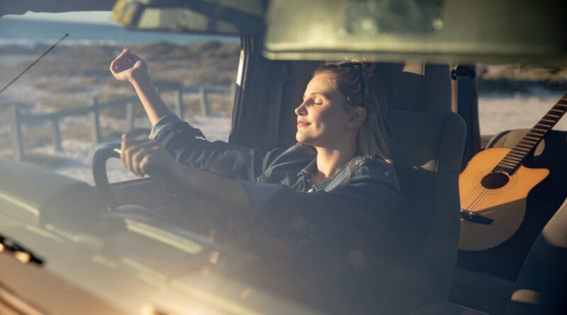 Vorderansicht einer kaukasischen Frau in einem offenen Top-Auto, hält ein Lenkrad, hob ihre Hände und entspannt in der Sonne mit geschlossenen Augen