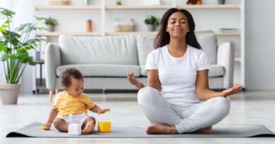 Mentales Wellness-Konzept. Ruhige glückliche schwarze Mutter meditiert mit Baby zu Hause, Afrikanische Dame sitzt in Lotusposition mit geschlossenen Augen, praktiziert Yoga im Wohnzimmer mit Kind, das herumspielt