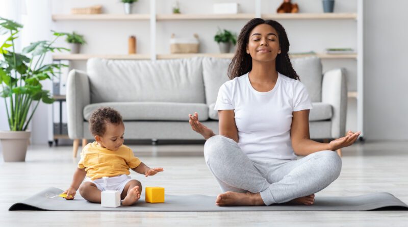 Mentales Wellness-Konzept. Ruhige glückliche schwarze Mutter meditiert mit Baby zu Hause, Afrikanische Dame sitzt in Lotusposition mit geschlossenen Augen, praktiziert Yoga im Wohnzimmer mit Kind, das herumspielt